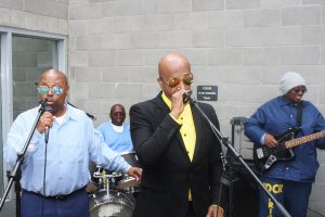 Singer MC Hammer sings into a microphone with inmates play instruments and sing backup.