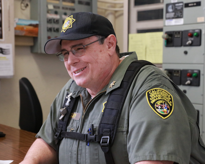 Man in uniform smiles while sitting at a desk.