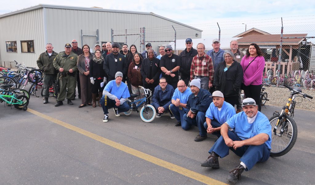 prison inmates, staff and volunteers stand near many refurbished bicycles.