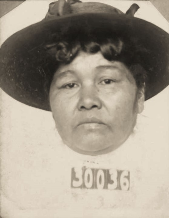 Woman wears a large hat with the numbers 30036 in her prison mugshot.