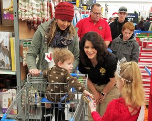 Boy in shopping cart reaches for candy canes while others watch.