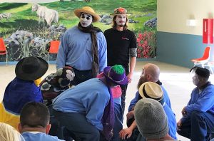 Prison inmates wear face paint and hats while rehearsing a scene.