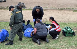 Prison medical staff huddle around a person on the ground while a correctional officer watches.
