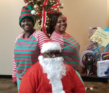 man in Santa outfit and two women in matching pajama style outfits.