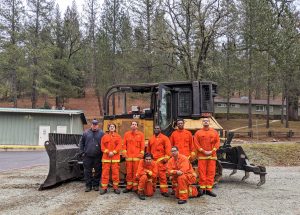 Seven inmate firefighters stand beside a large bulldozer.