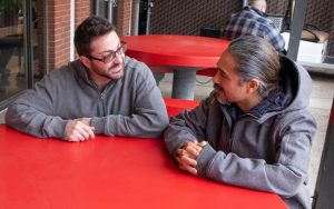 Two men sit at a red table.