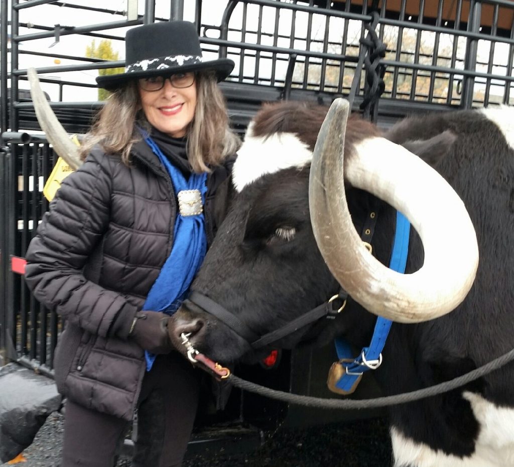 Woman in cowboy hat stands beside a longhorn steer.