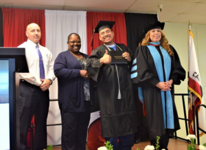 Two prison officials stand beside an inmate receiving a degree and a college superintendent.