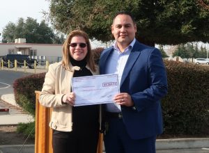 CDCR women's facility warden presents a check to Sisterhood of Survivors, a breast-cancer awareness organization. They are standing in the prison parking lot.