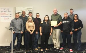 Men and women stand against a wall while holding a certificate.