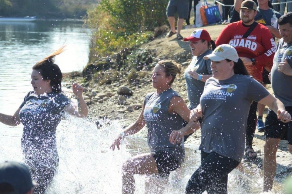 Women wearing Law Enforcement Torch Run shirts rush into cold water at Lake Natoma.