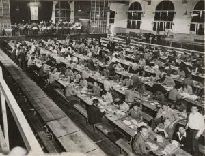 Incarcerated people sit in the mess hall sorting World War II ration books.