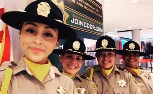 Four female correctional officers stand under a banner that reads JoinCDCR.com.