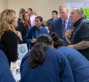 Women in blue surround an information table.