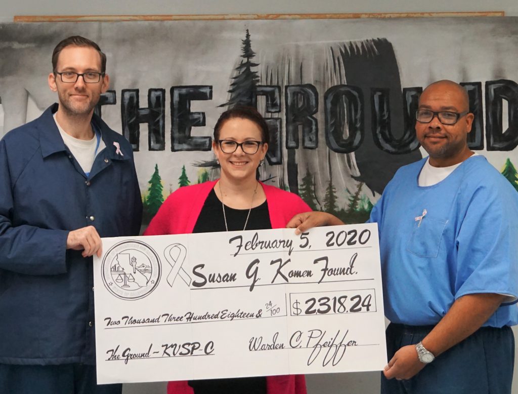 Two prison inmates and a woman hold an over-sized check.