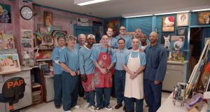 Men in blue stand in an art studio inside a prison.