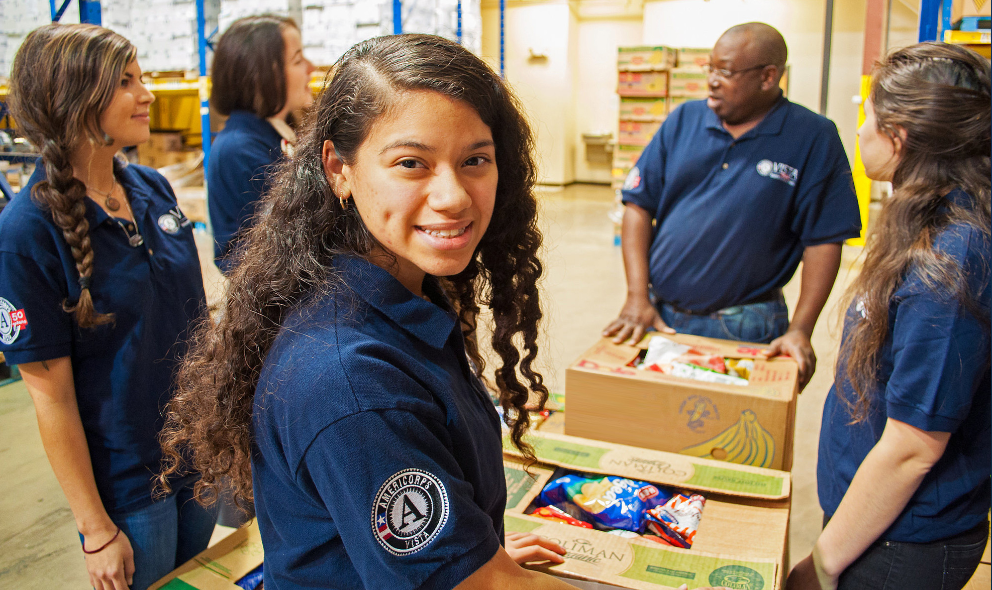 Volunteers in blue t-shirts pack boxes with food.