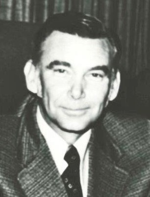 Man wearing vintage jacket and tie smiles at the camera.