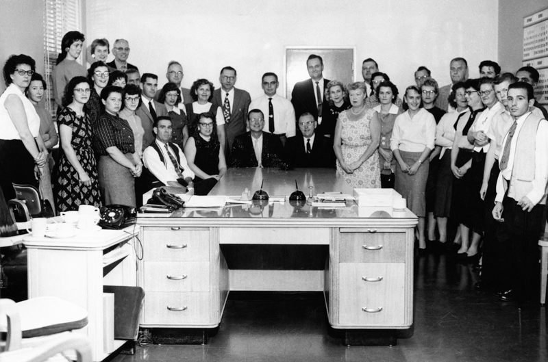 Men and women stand around a desk.