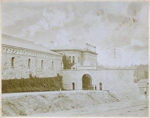 Gate in granite wall with other prison buildings in background.