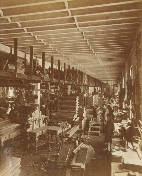 Long room with wooden roof, brick wall and piles of lumber.
