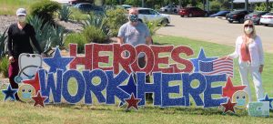 Photo of a man and two women wearing masks behind a sign that states: Heroes Work Here