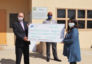 A large over-sized check is presented to a charity. Shown are two men and one woman, all wearing face coverings.
