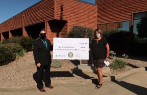 Two people hold an over-sized check while standing in front of a prison.