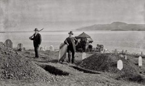Two men stand beside open graves.