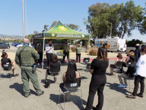 Men and women stand six feet apart and wear masks in the parking lot of a prison.
