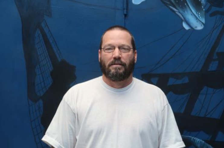 Man in white shirt stands in front of an undersea-themed mural.