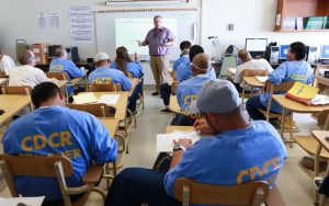 Students sit at desks while a teacher lectures in a classroom at Avenal State Prison.