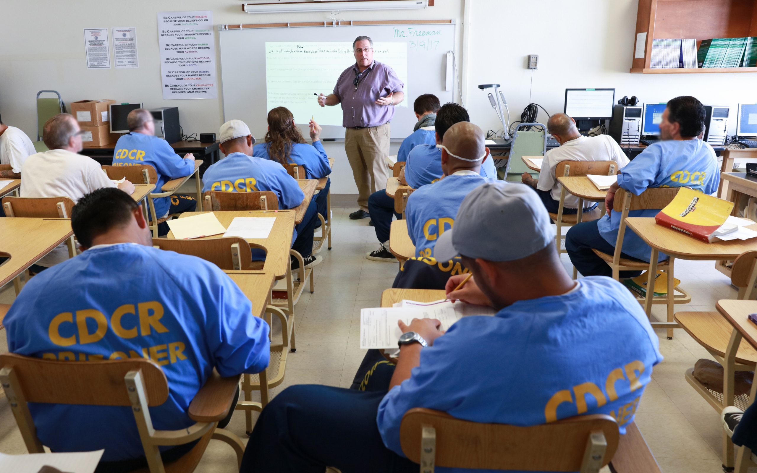 Students sit at desks while a teacher lectures in a classroom at Avenal State Prison.