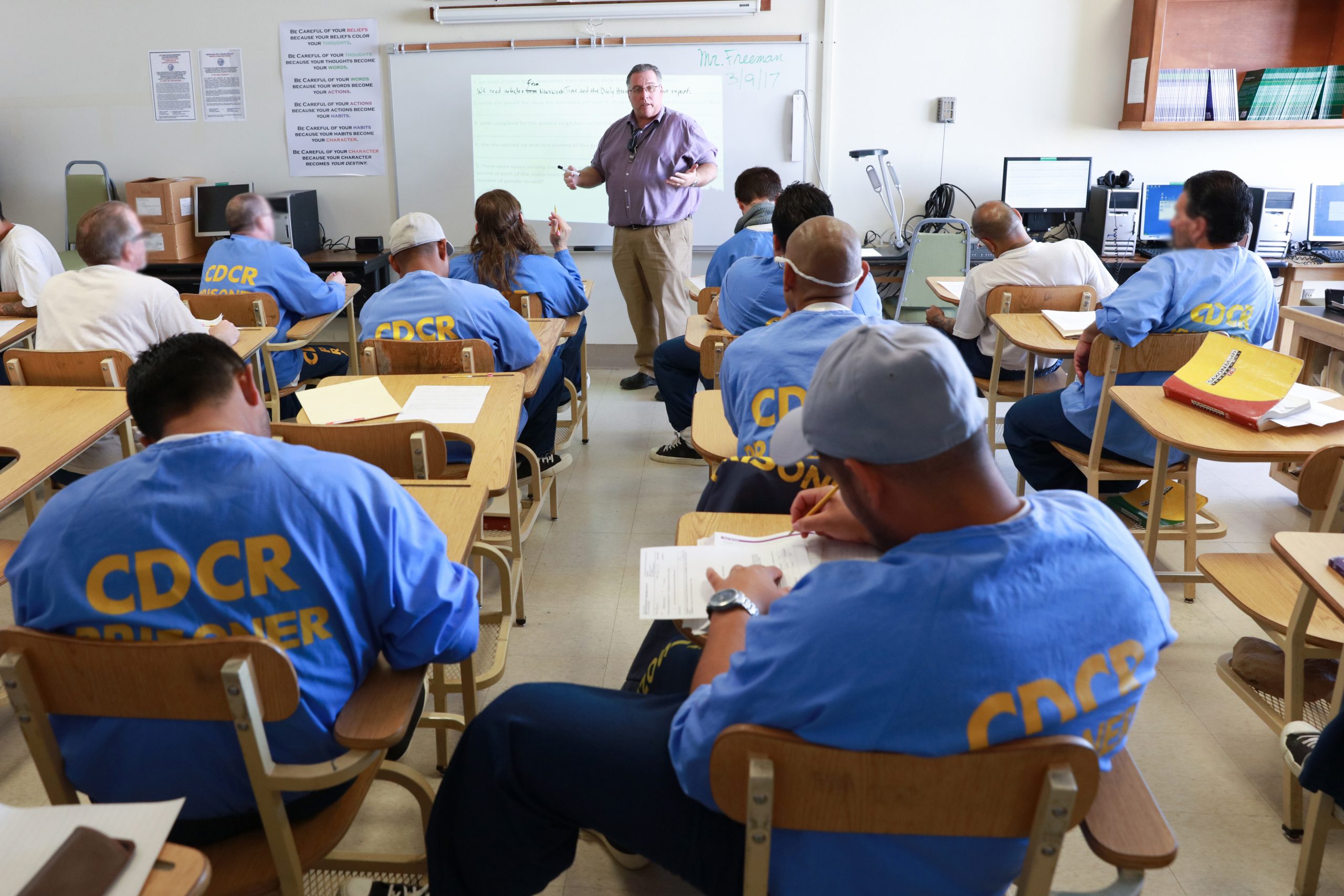 Students sit at desks while a teacher lectures in a classroom at Avenal State Prison.