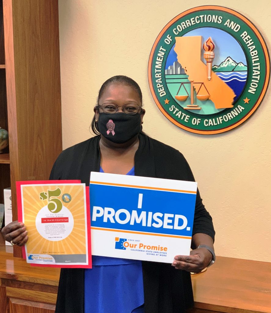 DAI Director Connie Gipson mask facing camera and holding Our Promise signs.