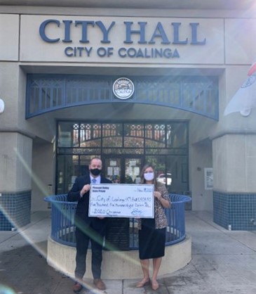 Two people hold an over-sized check in front of Coalinga City Hall.