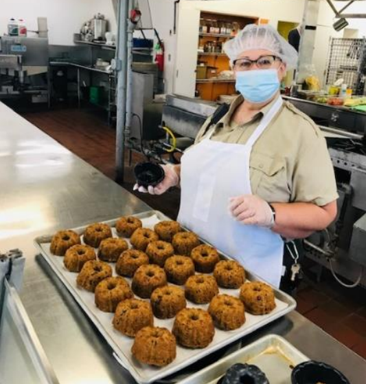 Supervising Cook Barbara Moreau stands beside a pan of small Bundt cakes in a prison camp kitchen.
