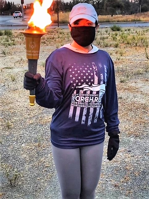 Woman wears a mask and carries the Special Olympics torch.