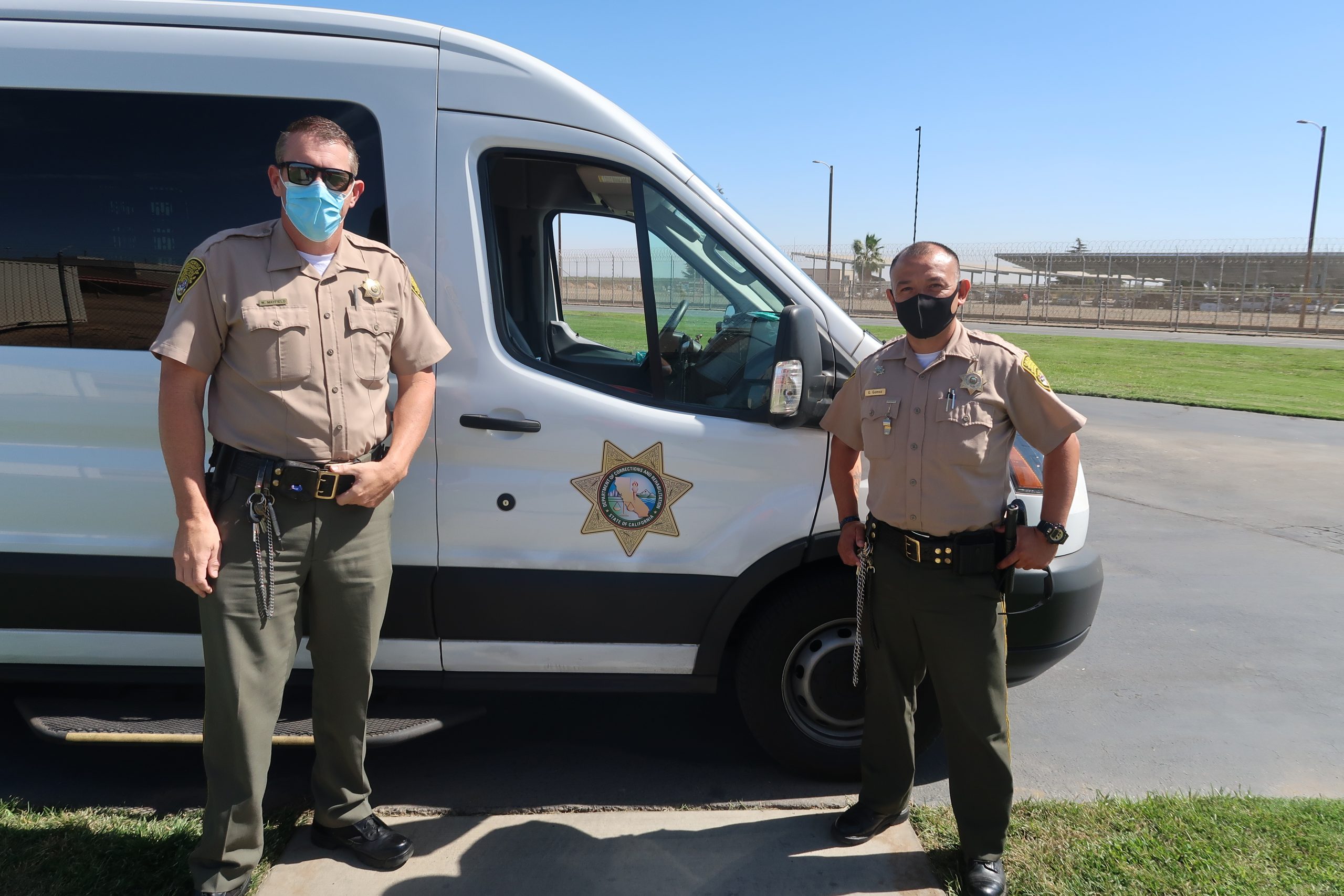 Correctional Officers Mayfield and Gomez stand in front of a CDCR transport .