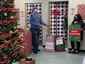 Three staff wear masks with holiday gifts, Christmas tree.