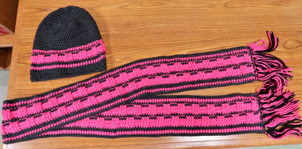 A pink hat and scarf knitted and crocheted by four people at Avenal State Prison.
