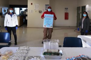 Helping accident victims' families, three prison staff people wearing masks and standing in front of table offering burritos and other food.