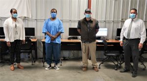A Cyber High student and staff at Avenal State Prison stand in front of computers.