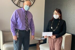 Centinela employee wears mask while handing a check to a masked woman at a food bank.