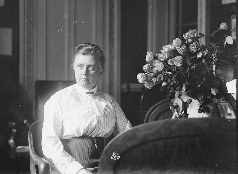 Woman sits in an office near flowers.