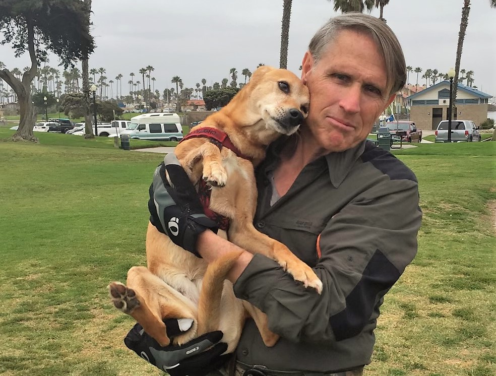 Bruce McGowan holds a dog while standing in a park.