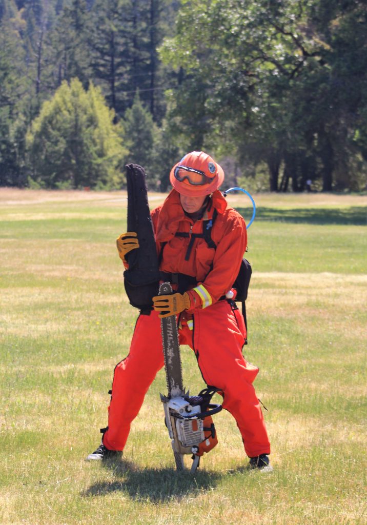 An orange-clad firefighter holds a chainsaw.