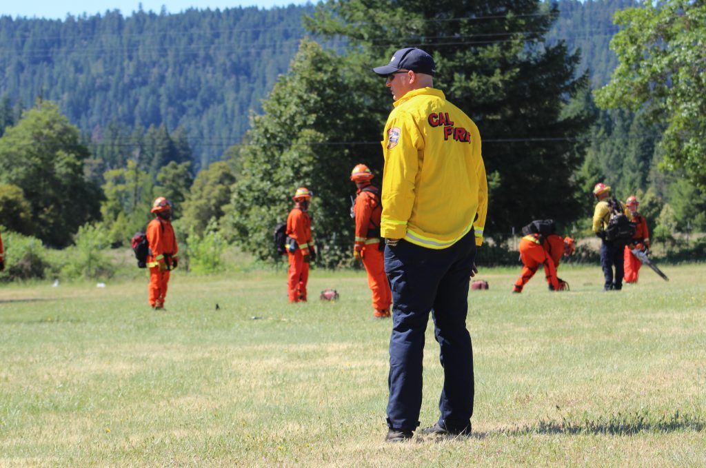 Firefighter in yellow observes others wearing orange. 
