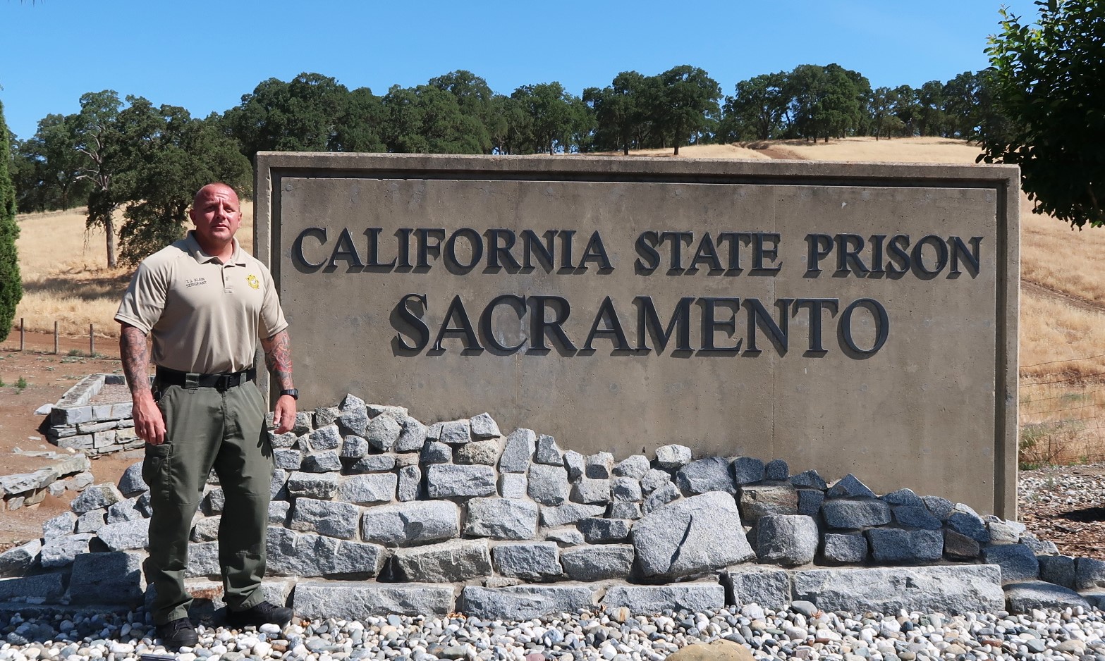 Correctional sergeant stands beside California State Prison Sacramento sign.