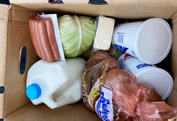 Milk, cabbage, potatoes, hot dogs and yogurt in a food box.
